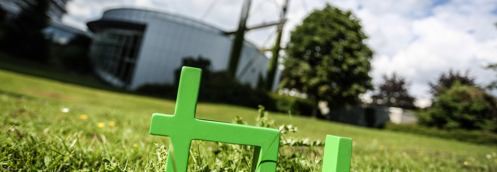Audimax TU Logo Im Vordergrund steht das TU Logo im Gras, im Hintergrund das Audimax.